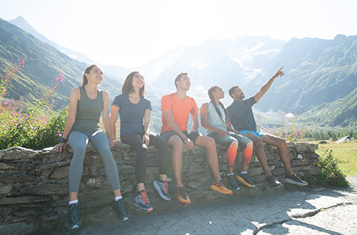 A group of friends sitting along the edge of a wall, modelling HOKA trainers.