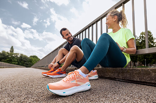 A man and a woman resting on a trail, modelling Brooks trainers.